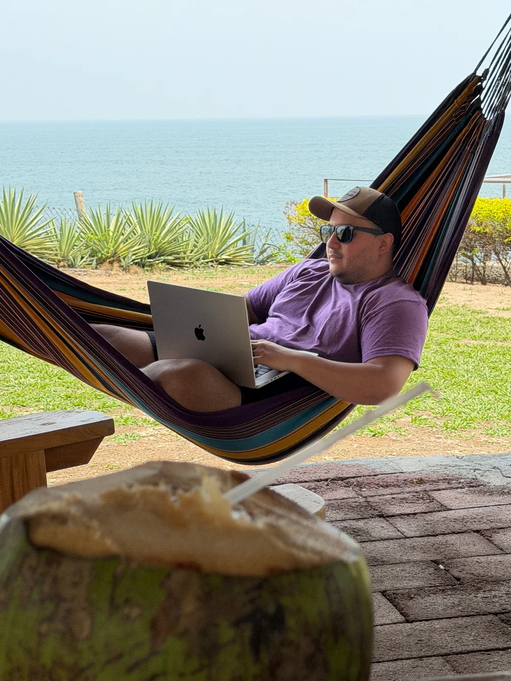 Working on a laptop in a hammock overlooking the ocean, with a fresh coconut in the foreground